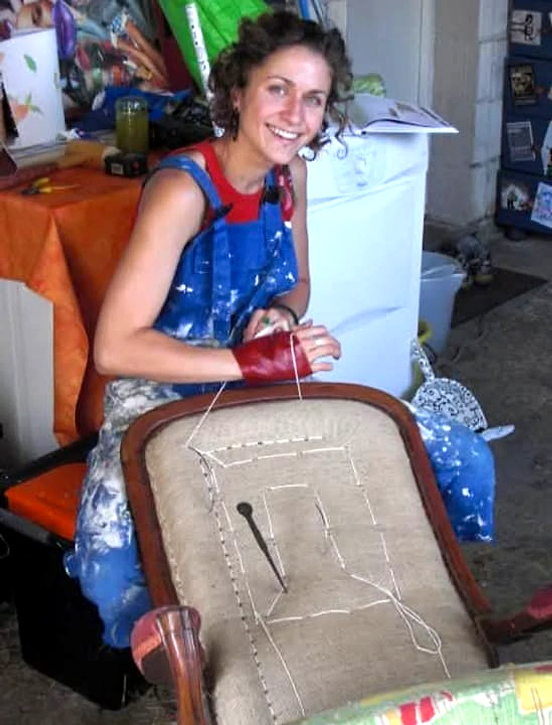 Sophie Aylmer, souriante dans son atelier, en train de garnir le dossier d'un siège
